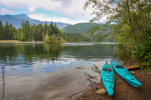 Hicks Lake in Sasquatch Provincial Park, BC. The view on two cyan - blue kayaks on the shore / beach. The trees and mountains in the background. photo