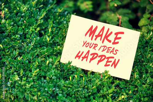 Motivational quote make your ideas happen written on paper in a garden with green plants in nature. Achievement or accomplishment in life or business. © Cagkan