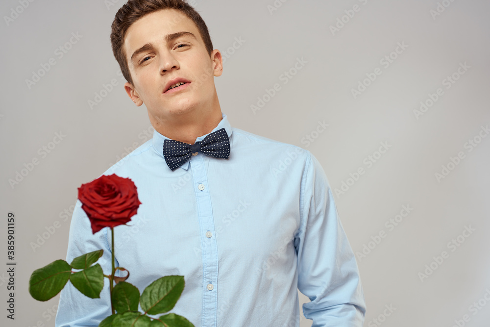 Handsome man with red rose blue shirt bow tie light background cropped view Handsome man with red rose blue shirt bow tie light background cropped view
