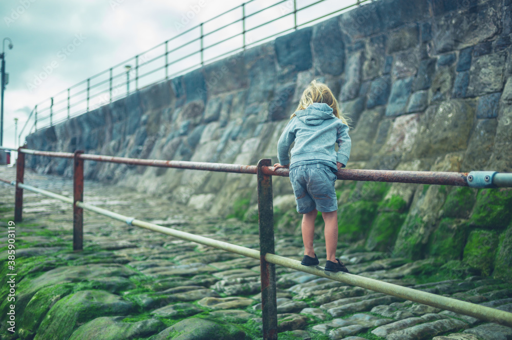 Preschooler playing by railing on the beach in autumn Preschooler playing by railing on the beach in autumn