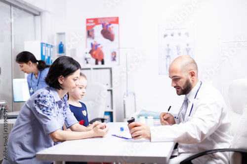 Doctor explaining treatment to mother of sick child in hospital office holding pills bottle. Healthcare physician specialist in medicine providing health care services treatment examination.