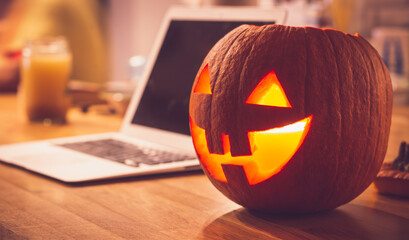 Lonely evening on Halloween. Laptop and lit pumpkin candle at home on the table. Concept of spending Halloween during the period of people's isolation during the coronavirus.