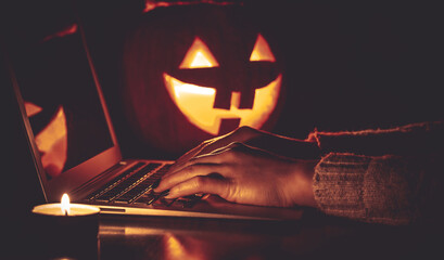 Halloween evening at the computer. Woman talking on the feast of Halloween on the internet. Coronavirus pandemic time concept. Shallow depth of field and noise.