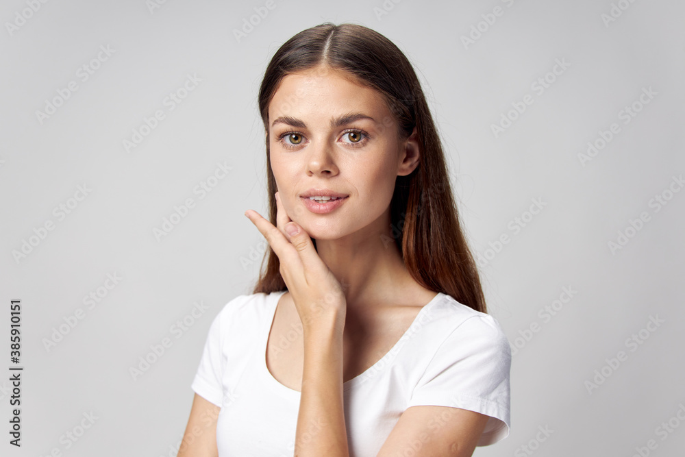Pretty woman touches her face with her hand and smiles on a light background Pretty woman touches her face with her hand and smiles on a light background