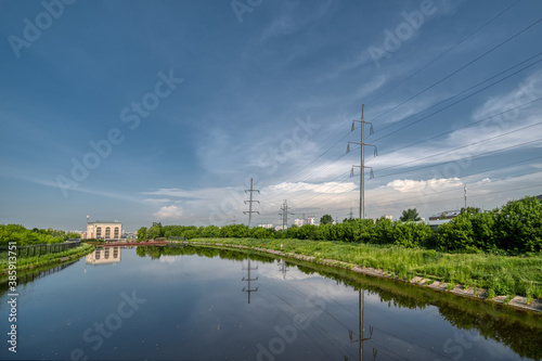 A small river, on the banks of the river there are high-voltage line towers