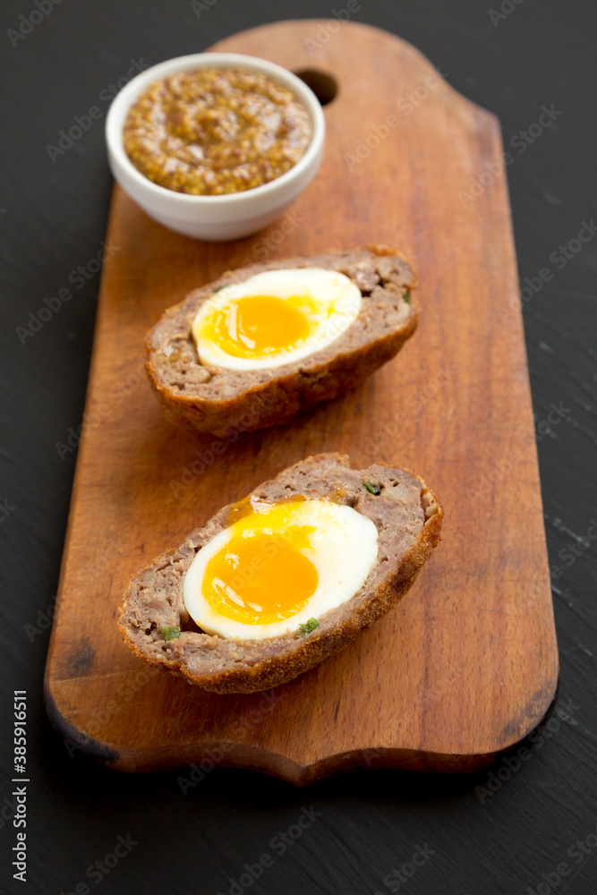 Homemade Scotch Eggs on a rustic wooden board on a black background, side view. Homemade Scotch Eggs on a rustic wooden board on a black background, side view.