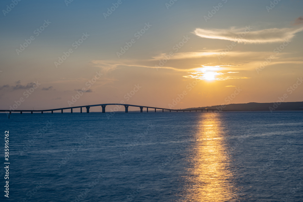 海辺で眺める沈む夕日と橋、宮古島・トゥリバーサンセットビーチ