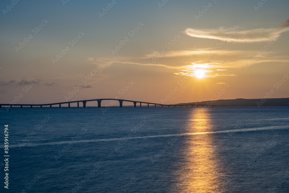 海辺で眺める沈む夕日と橋、宮古島・トゥリバーサンセットビーチ