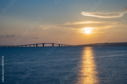 海辺で眺める沈む夕日と橋、宮古島・トゥリバーサンセットビーチ © Ryoma