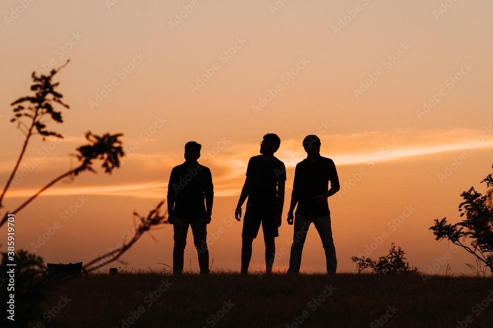 Silhouette of three Indian friends standing in front of the sky during the sunset Silhouette of three Indian friends standing in front of the sky during the sunset