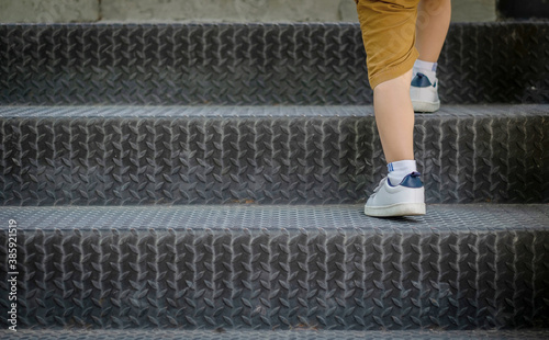 Close up of boy in sneaker shoe walking up outdoor metal stair. Child lifestyle successful concept.
