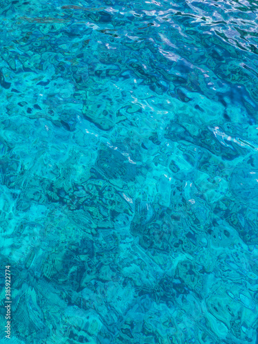 Crystal clear turquoise water surface with beautiful pattern. Sun light reflecting above waves. Blue natural background