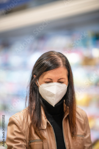Caucasian woman wearing face mask in the supermarket departmentstore. Girl choosing, looking grocery things to buy at shelf during coronavirus crisis or covid19 outbreak