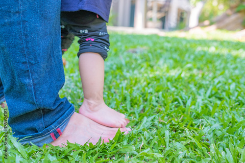 Father and baby legs standing on green grass. First steps walk. Selective focus. Background. 