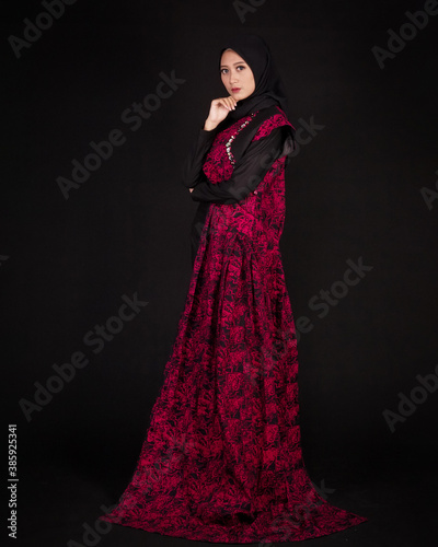 women in hijab are posing like famous models. The woman is wearing a typical Indonesian batik dress. The combination of modern dress designs with red batik that looks elegant.