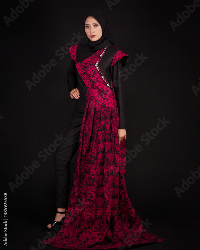 women in hijab are posing like famous models. The woman is wearing a typical Indonesian batik dress. The combination of modern dress designs with red batik that looks elegant.