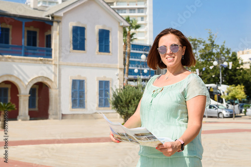 Portrait of a young smiling caucasian brunette woman in green dress and stylish sun flasses at the bright sunny day. Tourist woman with guide on the square in the center of Limassol, Cyprus. photo