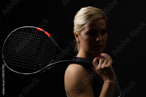Young female tennis player posing with racket on black background © Angelov
