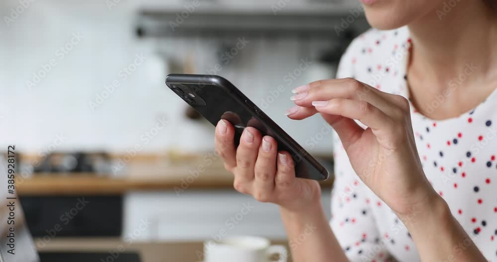 Close up view female standing in kitchen using smart phone modern device spend free time on internet, smile scrolling pictures on gadget, buy on e-services websites, modern wireless tech usage concept