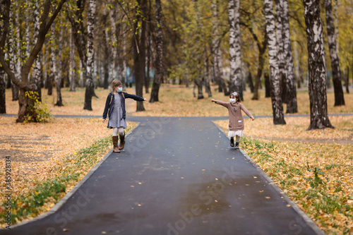 Fototapeta Naklejka Na Ścianę i Meble -  children girls friends walk in the park wearing masks, without touching, children walk keeping a distance, protection from the virus, social distance and friendship, quarantine and restrictions