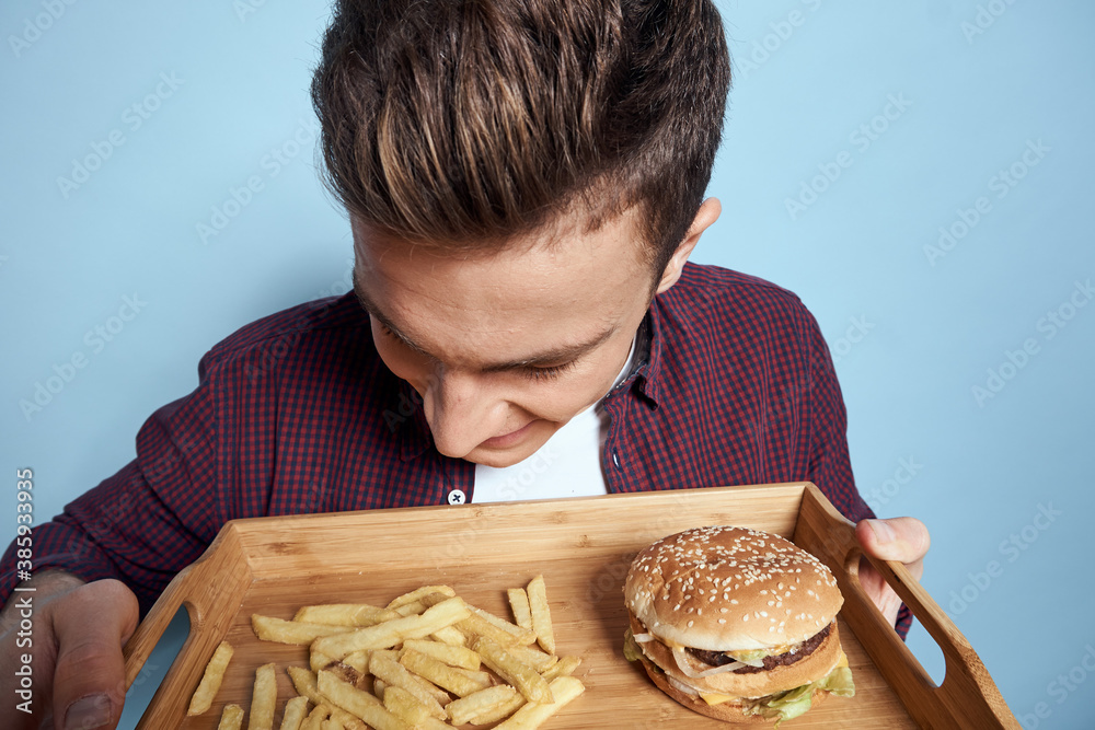 Man with wooden pallet fast food french fries hamburger hunger diet food blue background Man with wooden pallet fast food french fries hamburger hunger diet food blue background