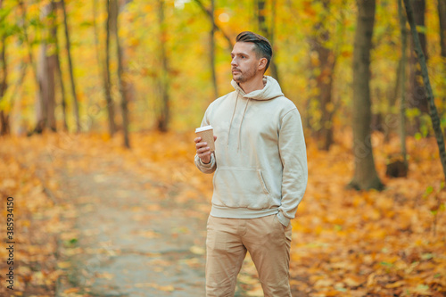 Young man drinking coffee in autumn park outdoors