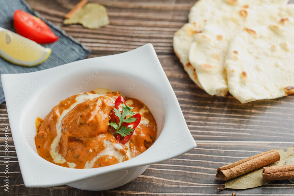 Butter chicken bowl and naan bread on wooden table. Curry - Meal, Indian food. Butter chicken bowl and naan bread on wooden table. Curry - Meal, Indian food.