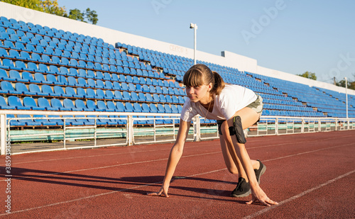 Young woman on starting position, getting ready to run at stadium track photo