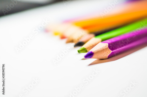 Colored pencils for drawing, well sharpened, lie in a row on a white background.