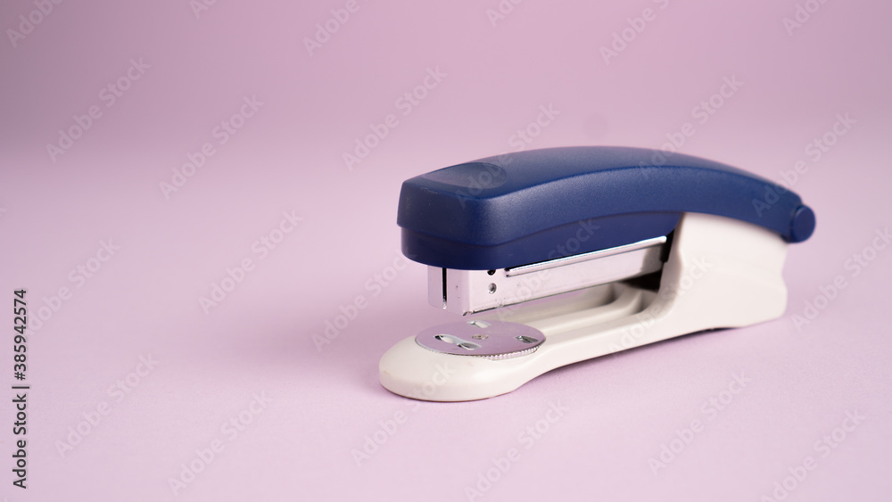 Blue stapler isolated on a purple background. Office supplies. Stapler, staple, paper, cardboard, office equipment Blue stapler isolated on a purple background. Office supplies. Stapler, staple, paper, cardboard, office equipment