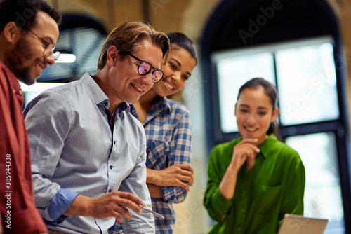 Positive male boss discussing project results and sharing ideas with young motivated multi ethnic team while standing together in the modern office