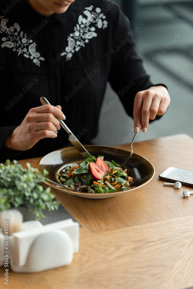 Vegan girl dines in a restaurant. Vegetable veggie salad garnished with fresh strawberries. Shallow depth of field, blurred background.
