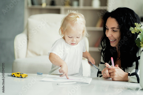 a young woman of European appearance ethnic group, playing with children's toys draw different markers, smart developing with her daughter a small child kids. beautiful bright and cozy apartment.