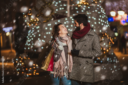 Young couple in the city centre with holiday's brights in background. Couple holding gift in a Christmas night.