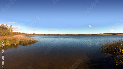 Quiet backwater on a rural lake with panoramic view of the village and forest far away on the horizon © DyMaxFoto