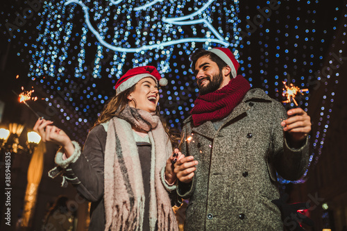 Romantic couple burning sparklers by holiday illumination on New Years eve.