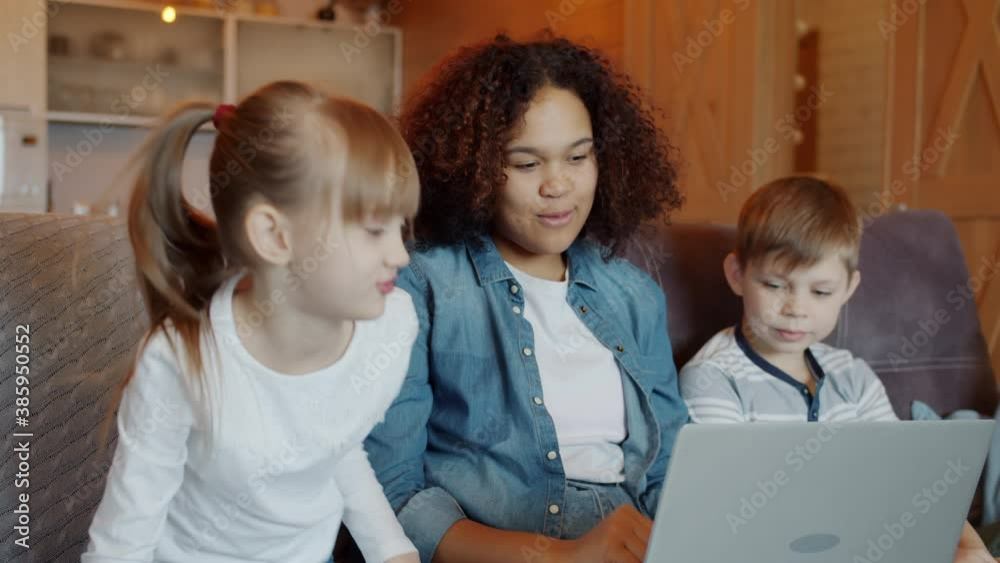Slow motion of friendly African American nanny talking to children boy and girl and using modern laptop at home. Technology and childcare concept. Slow motion of friendly African American nanny talking to children boy and girl and using modern laptop at home. Technology and childcare concept.