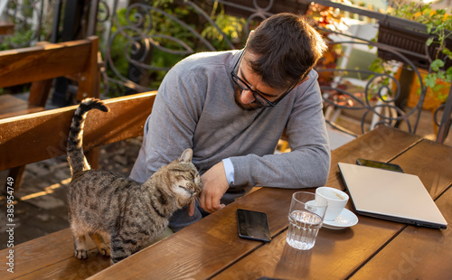 Businessman working in the coffee bar and playing with the cat
