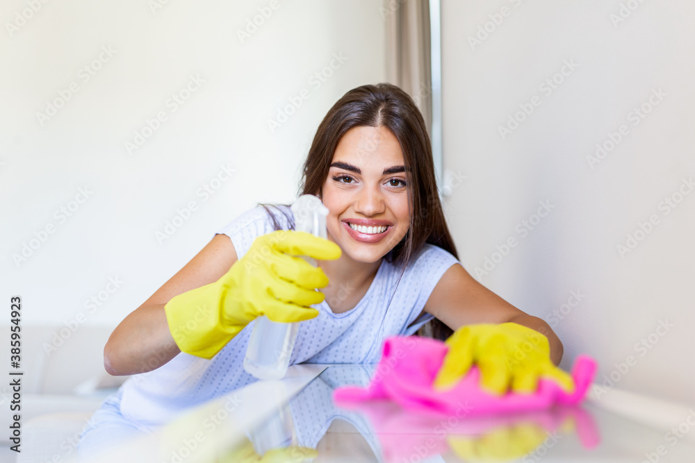 Beautiful young woman makes cleaning the house. Girl rubs dust. Smiling woman wearing rubber protective yellow gloves cleaning with rag and spray bottle detergent. Home, housekeeping concept. Beautiful young woman makes cleaning the house. Girl rubs dust. Smiling woman wearing rubber protective yellow gloves cleaning with rag and spray bottle detergent. Home, housekeeping concept.