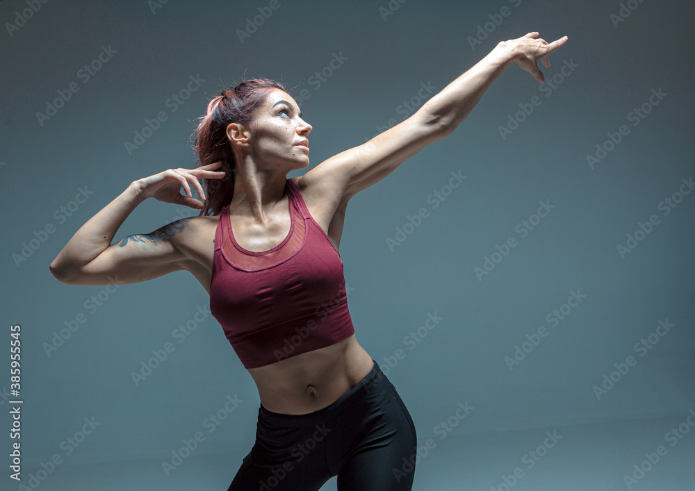 Portrait of a modern young girl performing elements of contemporary dance on a gray background.