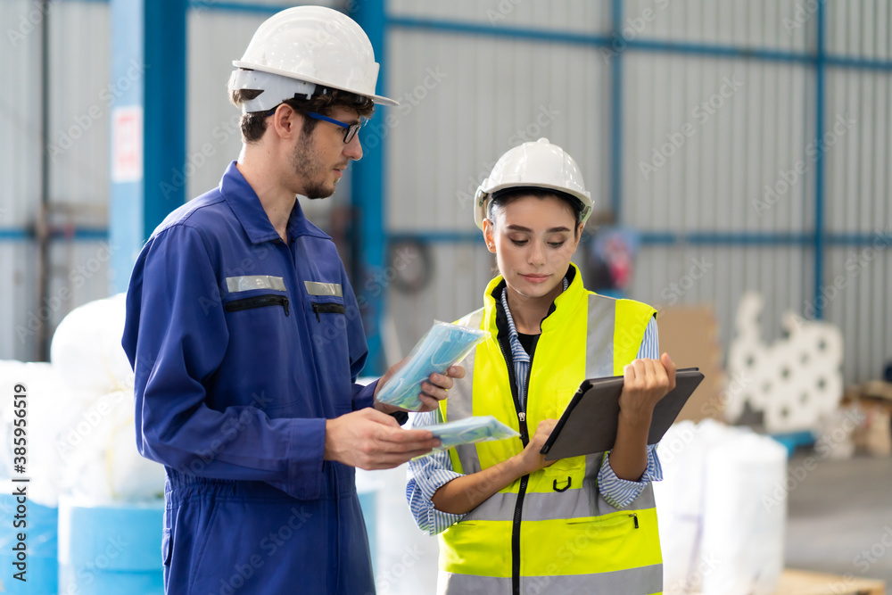 Female Inventory Manager checking stock on Digital Tablet. Man warehouse worker with hard hat safety helmet at storage buildings Female Inventory Manager checking stock on Digital Tablet. Man warehouse worker with hard hat safety helmet at storage buildings