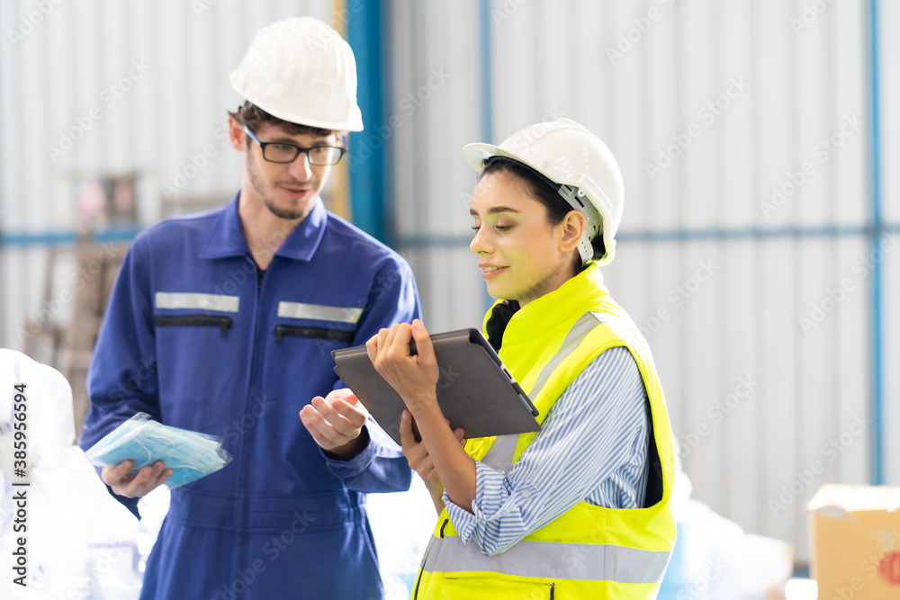 Female Inventory Manager checking stock on Digital Tablet. Man warehouse worker with hard hat safety helmet at storage buildings Female Inventory Manager checking stock on Digital Tablet. Man warehouse worker with hard hat safety helmet at storage buildings