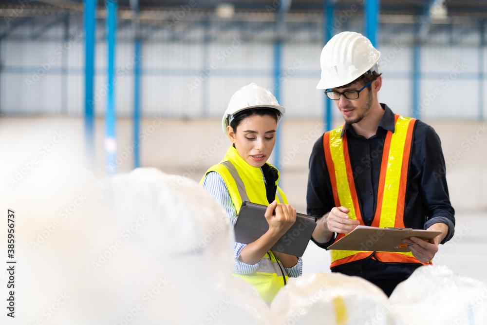 Obraz premium Female Inventory Manager checking stock on Digital Tablet. Man warehouse worker with hard hat safety helmet at storage buildings