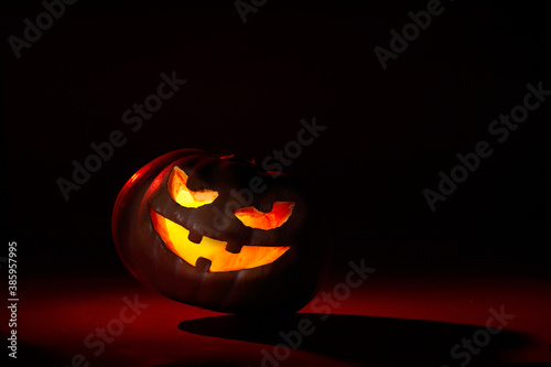 illuminated halloween pumpkin with leaning evil face on a dark background in red tones