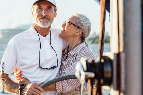 Mature woman looking and embracing on her husband while he steering a sailboat