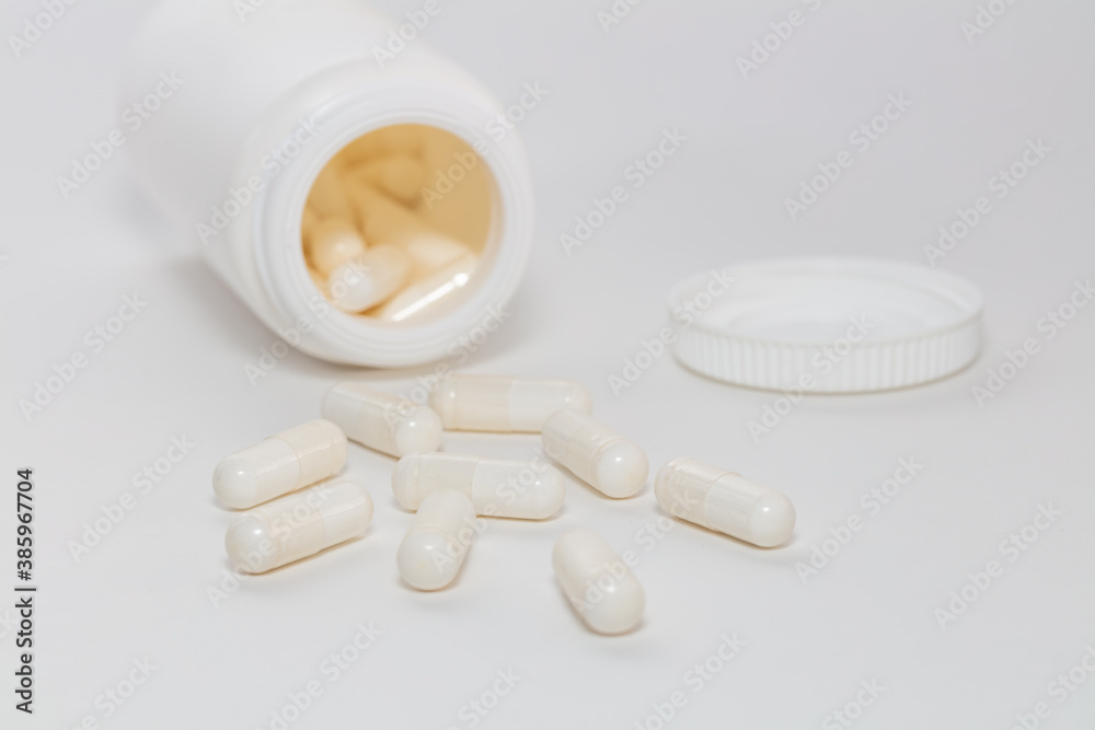 Bunch of white scattered pills on white background. White pills container and cap next to them slightly out of focus in the background. Close up. Pharmaceutical business and medicine sale concepts. Bunch of white scattered pills on white background. White pills container and cap next to them slightly out of focus in the background. Close up. Pharmaceutical business and medicine sale concepts.