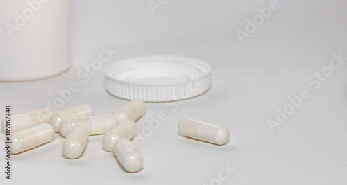 Bunch of white scattered pills on white background. White pills container and cap next to them slightly out of focus in the background. Close up. Pharmaceutical business and medicine sale concepts.