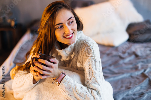 Young girl wrapped in a white blanket drinking coffee in a warm atmosphere. looking thoughtfully aside