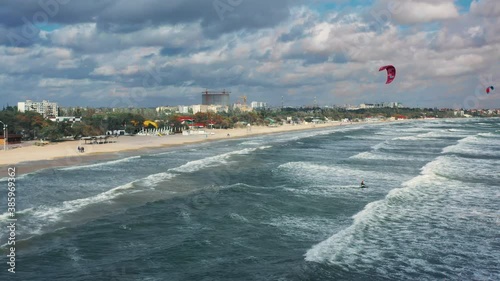 Riding big waves on kitesurfing in summer. 4K Drone view of the ocean and people engaged in extreme sports, kite surfing. Beautiful clear water Aerial view people kiteboarding ride.