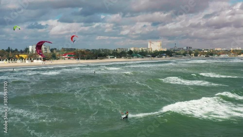 Riding big waves on kitesurfing in summer. 4K Drone view of the ocean and people engaged in extreme sports, kite surfing. Beautiful clear water Aerial view people kiteboarding ride.